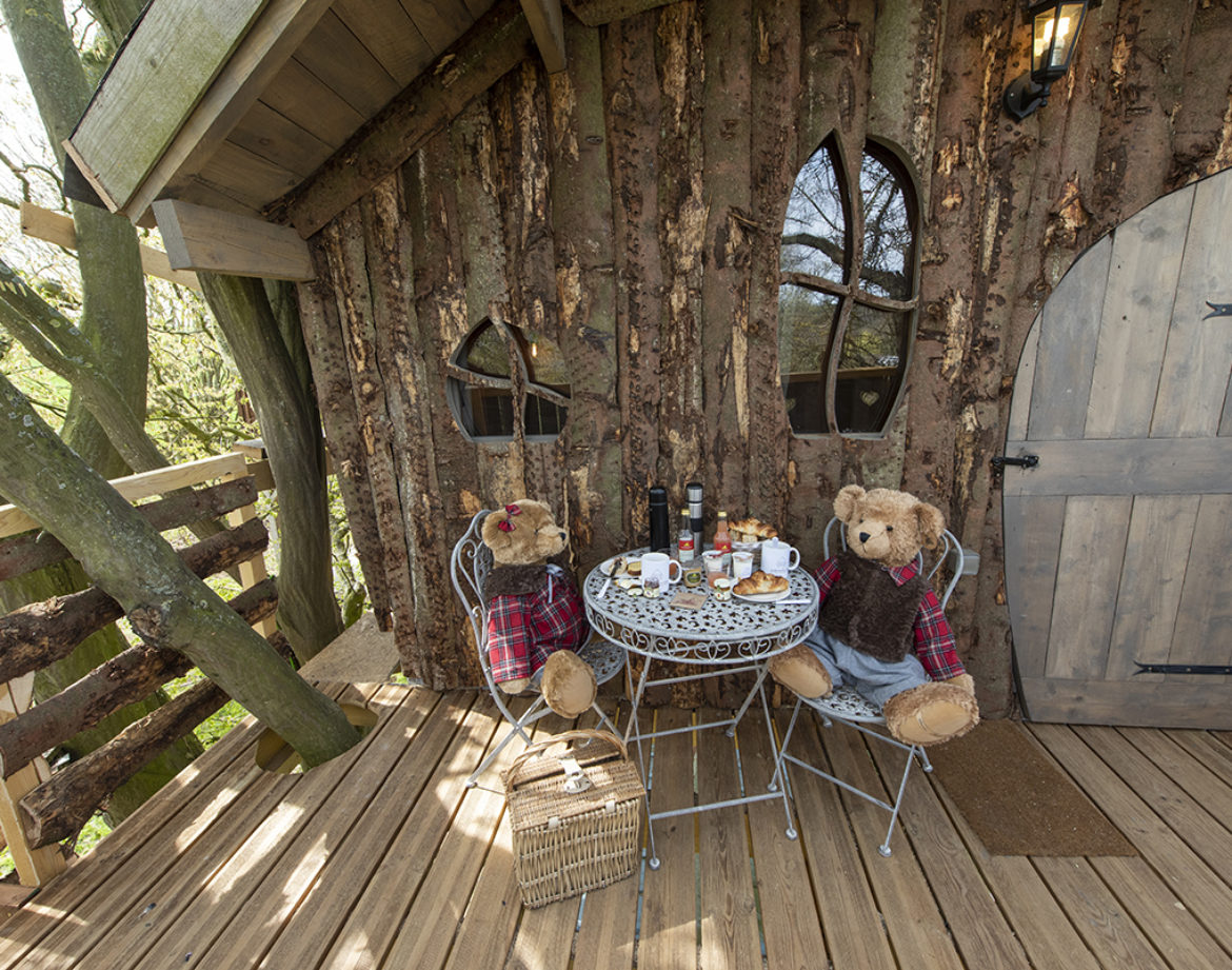Cabane en bois perchée, décorée de peluches, avec une table pour le petit-déjeuner.