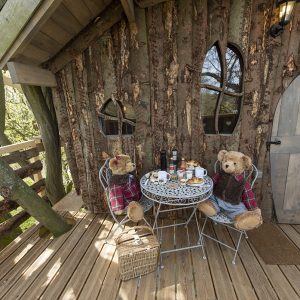 Cabane en bois perchée, décorée de peluches, avec une table pour le petit-déjeuner.