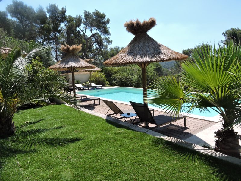Villa avec piscine, chaises longues et parasols au milieu dun jardin verdoyant.