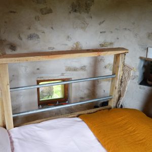 Chambre atypique en pierre avec lit en bois et fenêtre offrant une vue sur la nature.