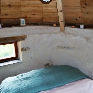 Chalet en bois avec murs en pierre, lit douillet et fenêtres lumineuses.