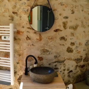 Salle de bain dun hébergement insolite en pierre, avec un lavabo en pierre et un miroir rond.