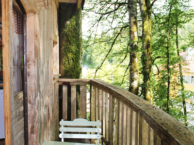 Cabane perchée en bois avec balcon, entourée darbres verdoyants en Bourgogne-Franche-Comté.