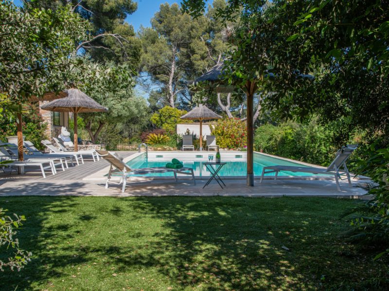 Villa avec piscine, entourée de verdure et de chaises longues confortables.
