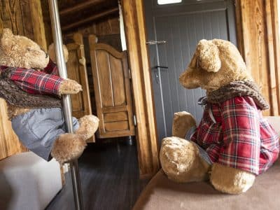 Hébergement insolite en bois avec des peluches sur un poteau et un lit confortable.