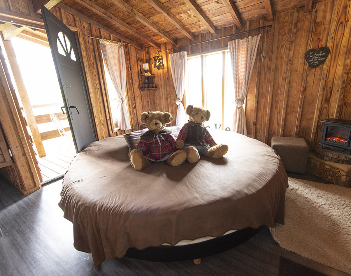 Cabane en bois cosy avec lit rond et ours en peluche sur la couette.