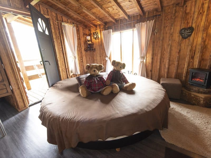 Cabane en bois cosy avec lit rond et ours en peluche sur la couette.
