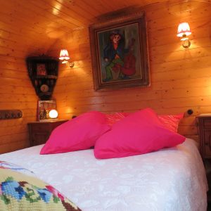 Chambre dhôtes en roulotte, bois chaleureux et coussins roses accueillants.