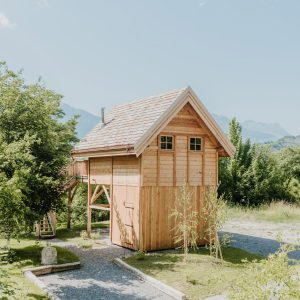 Cabane en bois sur pilotis, entourée de verdure et avec vue sur les montagnes.