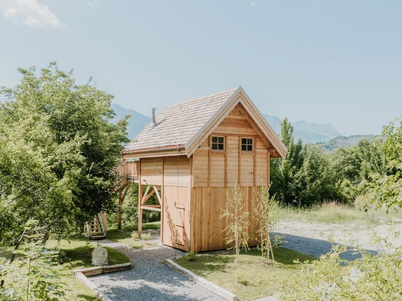 Charmante cabane en bois sur pilotis, entourée de verdure et de montagnes.