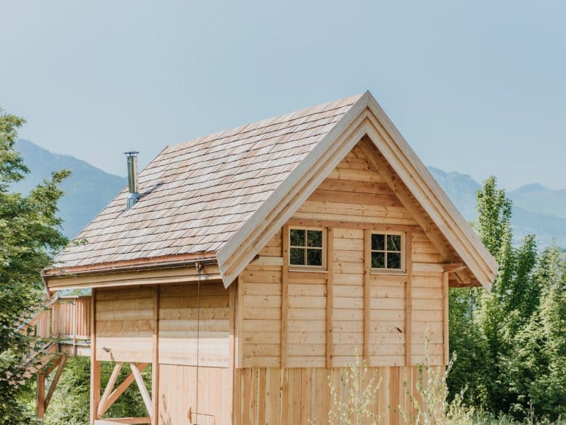 Charmante cabane en bois avec un toit en ardoise, entourée de verdure.