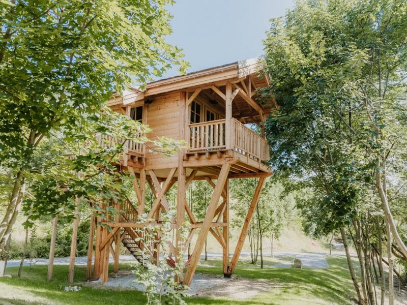Cabane en bois sur pilotis, entourée darbres verdoyants et dun escalier en bois.