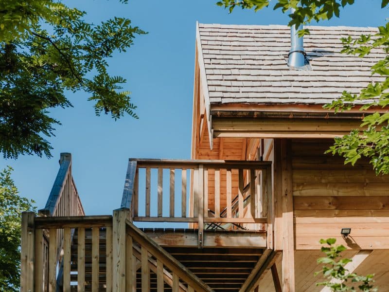 Cabane en bois perchée, avec balcon en bois et ciel bleu en toile de fond.