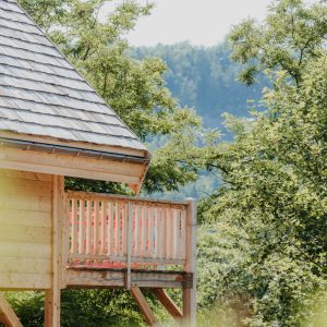 Cabane en bois perchée, entourée de verdure, avec un balcon offrant une vue dégagée.