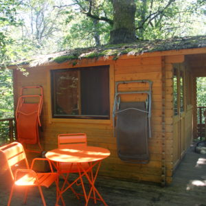Cabane en bois dans les arbres avec terrasse et mobilier orange.