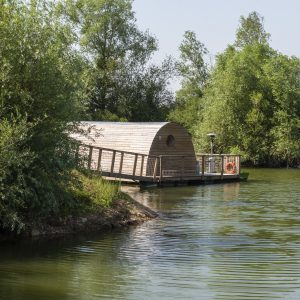 Hébergement insolite : cabane flottante en bois sur un lac verdoyant en Bourgogne.