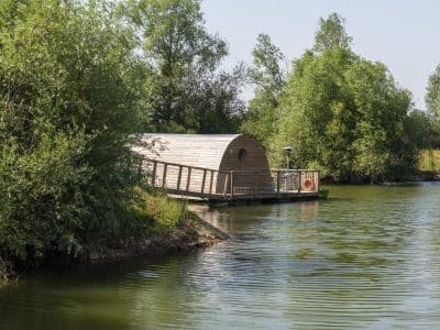 Hébergement insolite : cabane flottante en bois sur un lac verdoyant en Bourgogne.