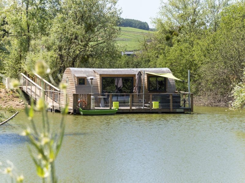 Cabane flottante en Bourgogne, entourée de verdure et accessible par une passerelle.