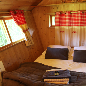Chalet en bois cosy avec lit douillet et rideaux à carreaux en Bourgogne-Franche-Comté.