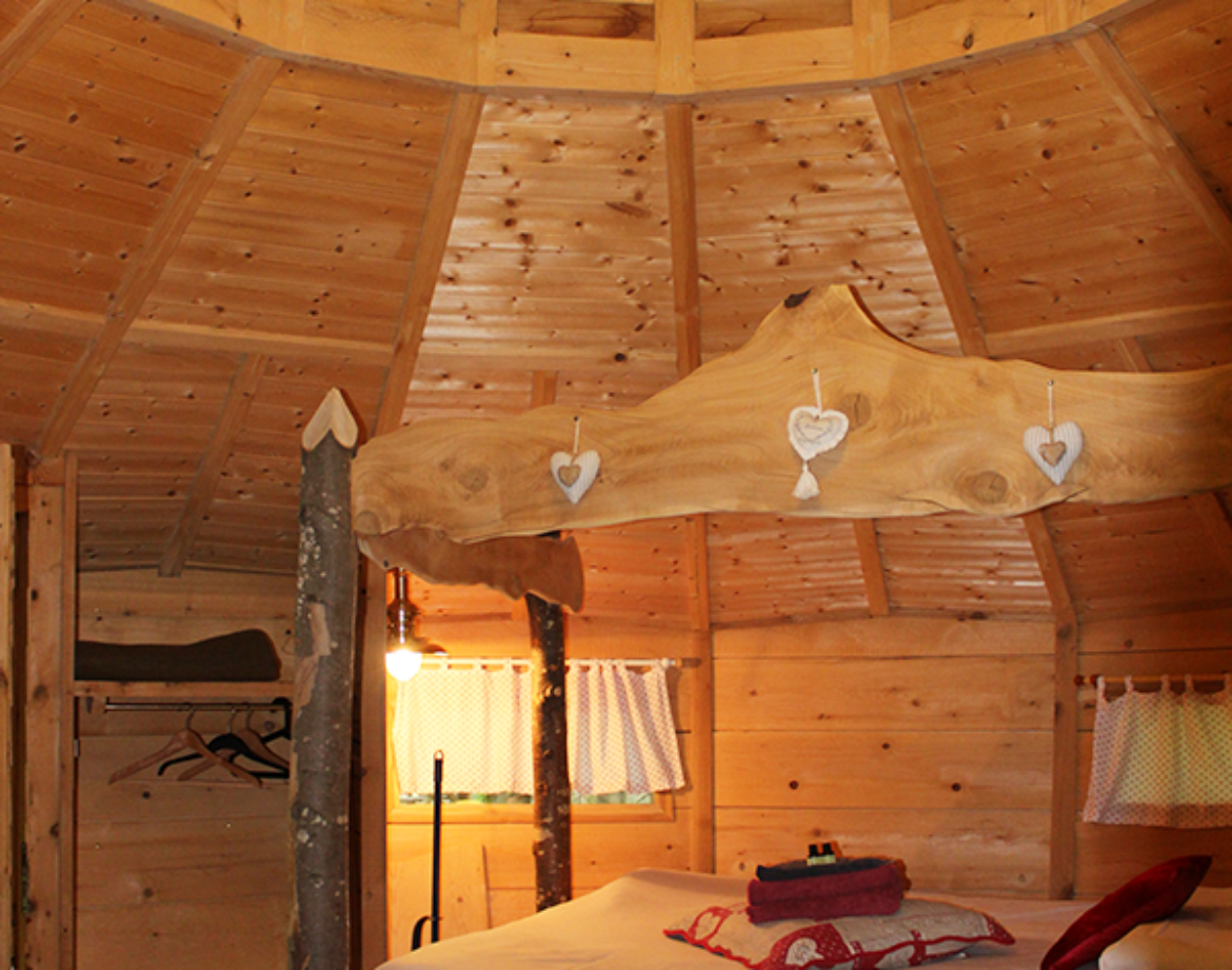 Hébergement insolite en cabane ronde, intérieur en bois avec lit douillet et lumière douce.