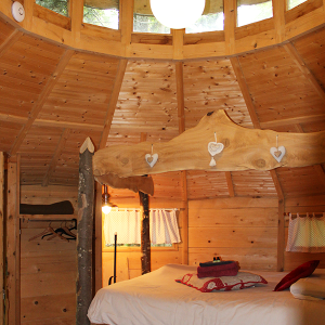 Hébergement insolite en cabane ronde, intérieur en bois avec lit douillet et lumière douce.