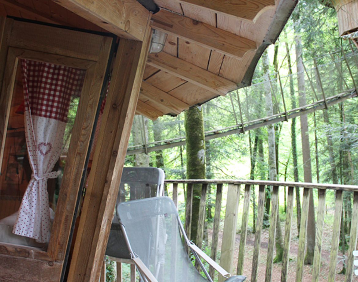 Cabane perchée en bois avec terrasse, entourée darbres verdoyants en Bourgogne-Franche-Comté.