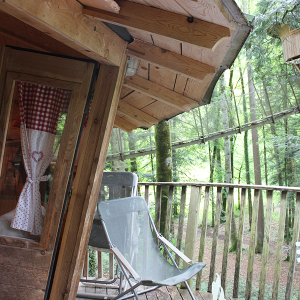 Cabane perchée en bois avec terrasse, entourée darbres verdoyants en Bourgogne-Franche-Comté.