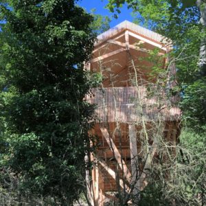 Cabane perchée en bois, entourée de verdure, offrant une vue imprenable sur la nature.