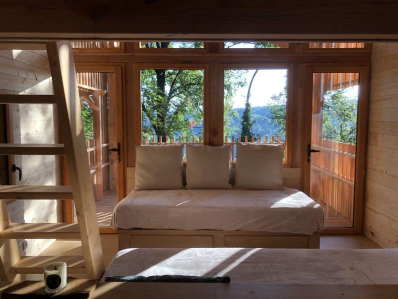 Cabane en bois avec grandes fenêtres offrant une vue sur la nature environnante.