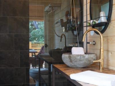 Salle de bain moderne dun hébergement insolite en bois, avec douche en verre et lavabo en pierre.