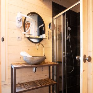 Salle de bain moderne en bois, avec douche et lavabo en pierre, dans un hébergement insolite.