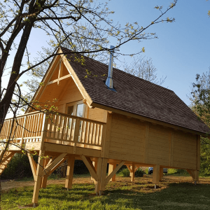 Cabane en bois perchée, entourée de verdure, avec un balcon ensoleillé.
