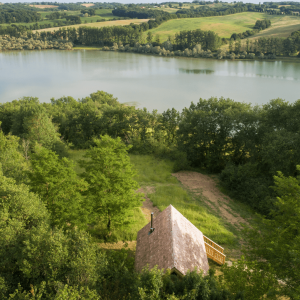 Cabane en bois au bord dun lac, entourée de verdure et de paysages vallonnés.