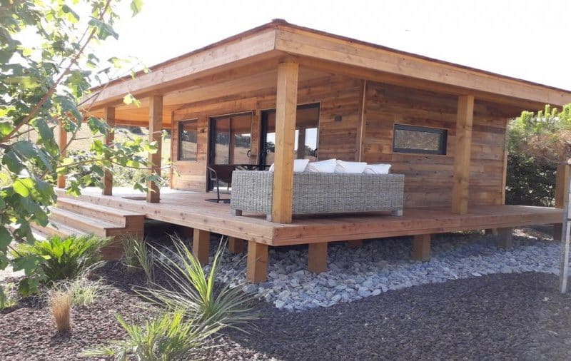 Chalet en bois avec terrasse, entouré de verdure et de galets décoratifs.