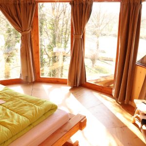 Cabane en bois avec grandes fenêtres et lit douillet, vue sur la nature.