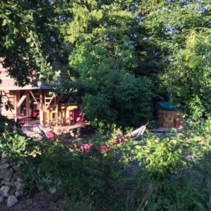 Cabane en bois entourée de verdure, avec un hamac et un espace détente.