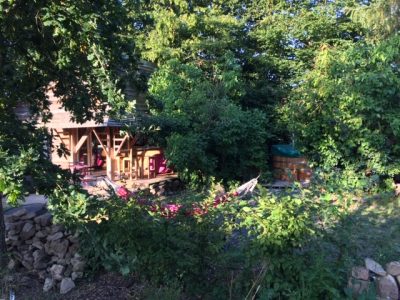 Cabane en bois entourée de verdure, avec un hamac et un espace détente.