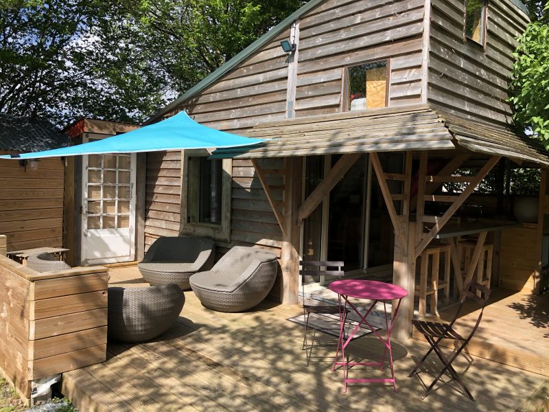 Charmante cabane en bois avec terrasse ensoleillée et mobilier confortable.