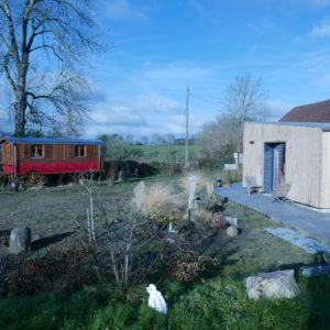 Hébergement insolite en roulotte rouge et chalet en bois, entouré de verdure.