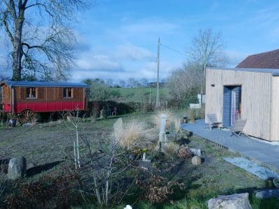 Hébergement insolite en roulotte rouge et chalet en bois, entouré de verdure.