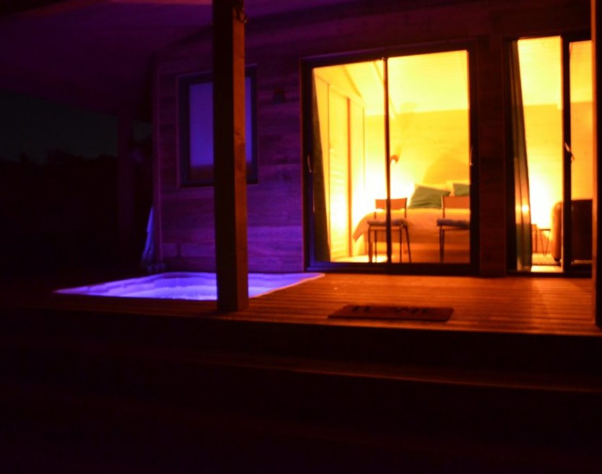 Cabane insolite avec jacuzzi, éclairage chaleureux et ambiance nocturne apaisante.