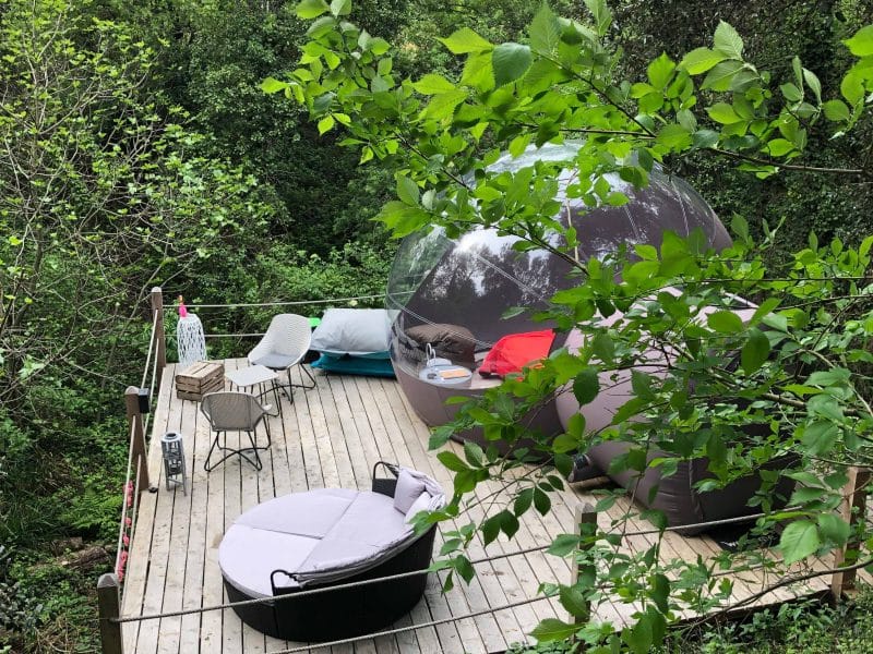 Bulle transparente sur une terrasse en bois, entourée de verdure luxuriante.