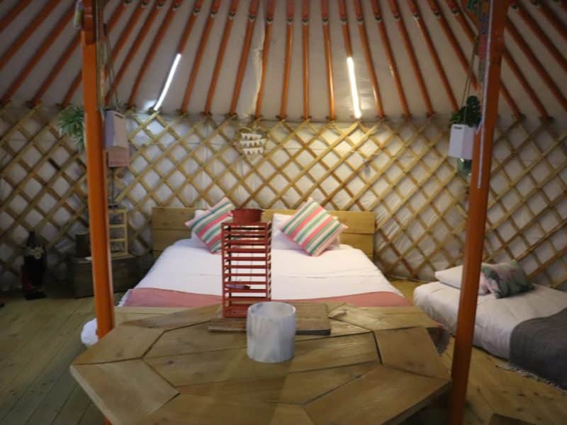 Yourte chaleureuse avec lit douillet et décoration colorée, ambiance cosy et naturelle.