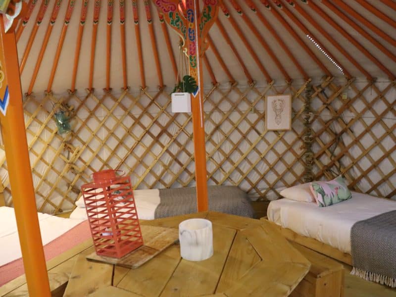 Yourte chaleureuse avec lits confortables et décoration colorée en bois.