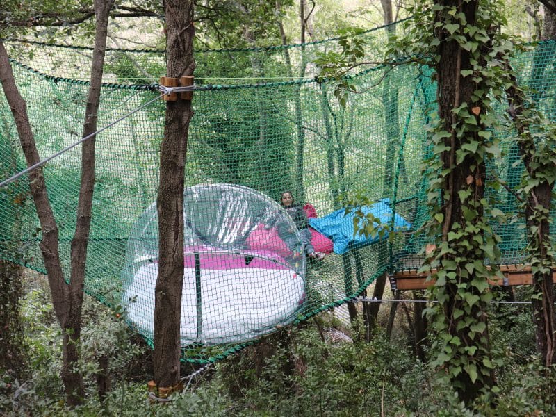 Hébergement insolite : bulle suspendue dans les arbres, entourée de verdure.