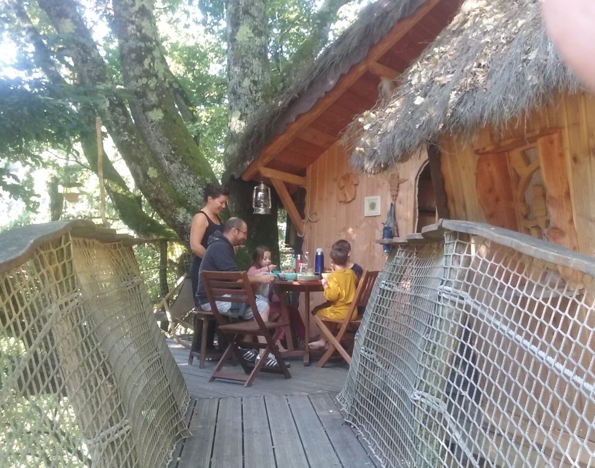 Cabane dans les arbres en Auvergne-Rhône-Alpes, avec terrasse en bois et famille réunie.