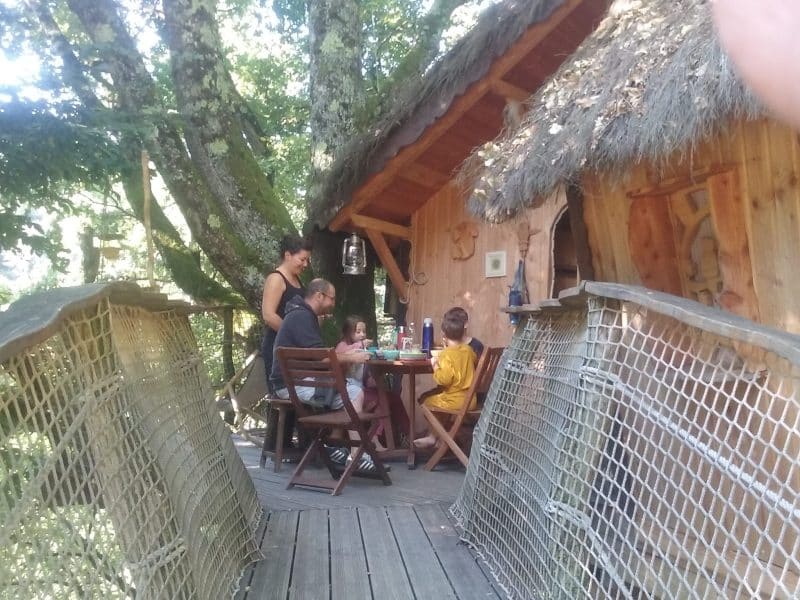 Cabane dans les arbres, famille réunie autour dune table en bois sur la terrasse.