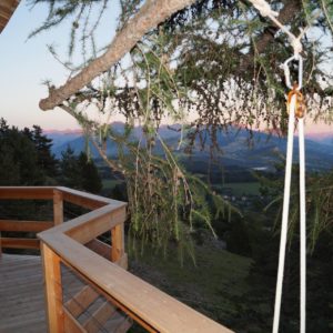 Cabane perchée avec terrasse en bois, vue panoramique sur les montagnes.