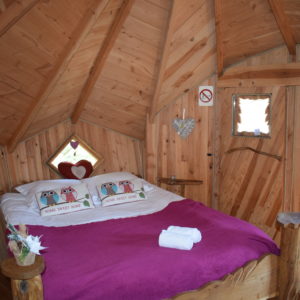 Cabane en bois en Bretagne, lit douillet avec coussins décoratifs et ambiance chaleureuse.