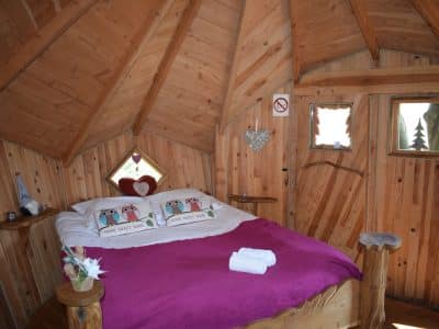 Cabane en bois en Bretagne, lit douillet avec coussins décoratifs et ambiance chaleureuse.